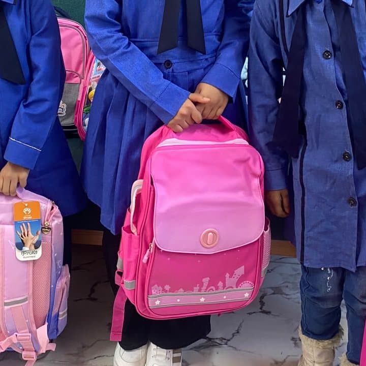 Students in school uniform holding new pink backpacks
